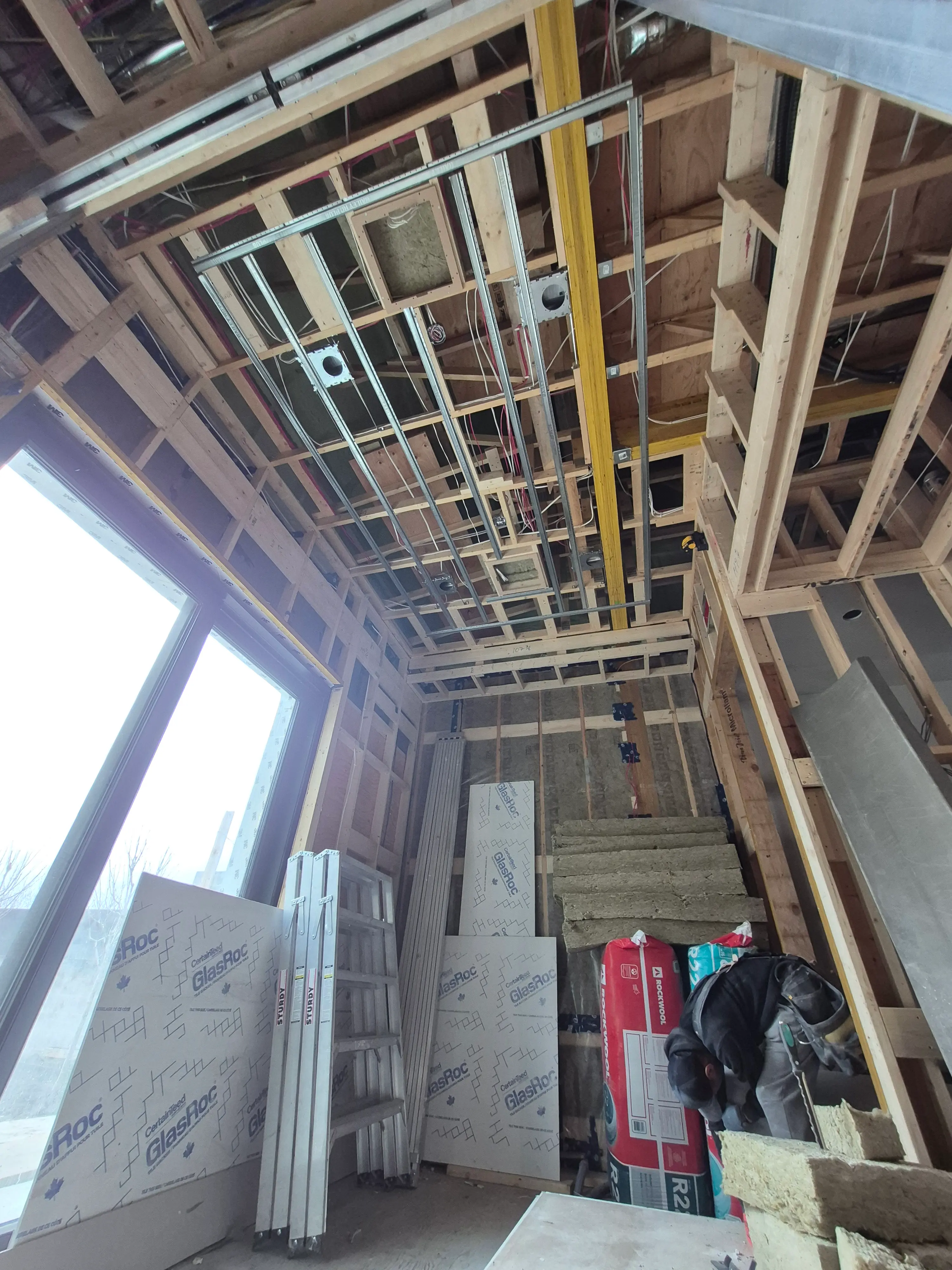 Interior room under construction with unfinished drywall, a large sliding glass door, a yellow scaffolding, and a floor covered in protective sheets.