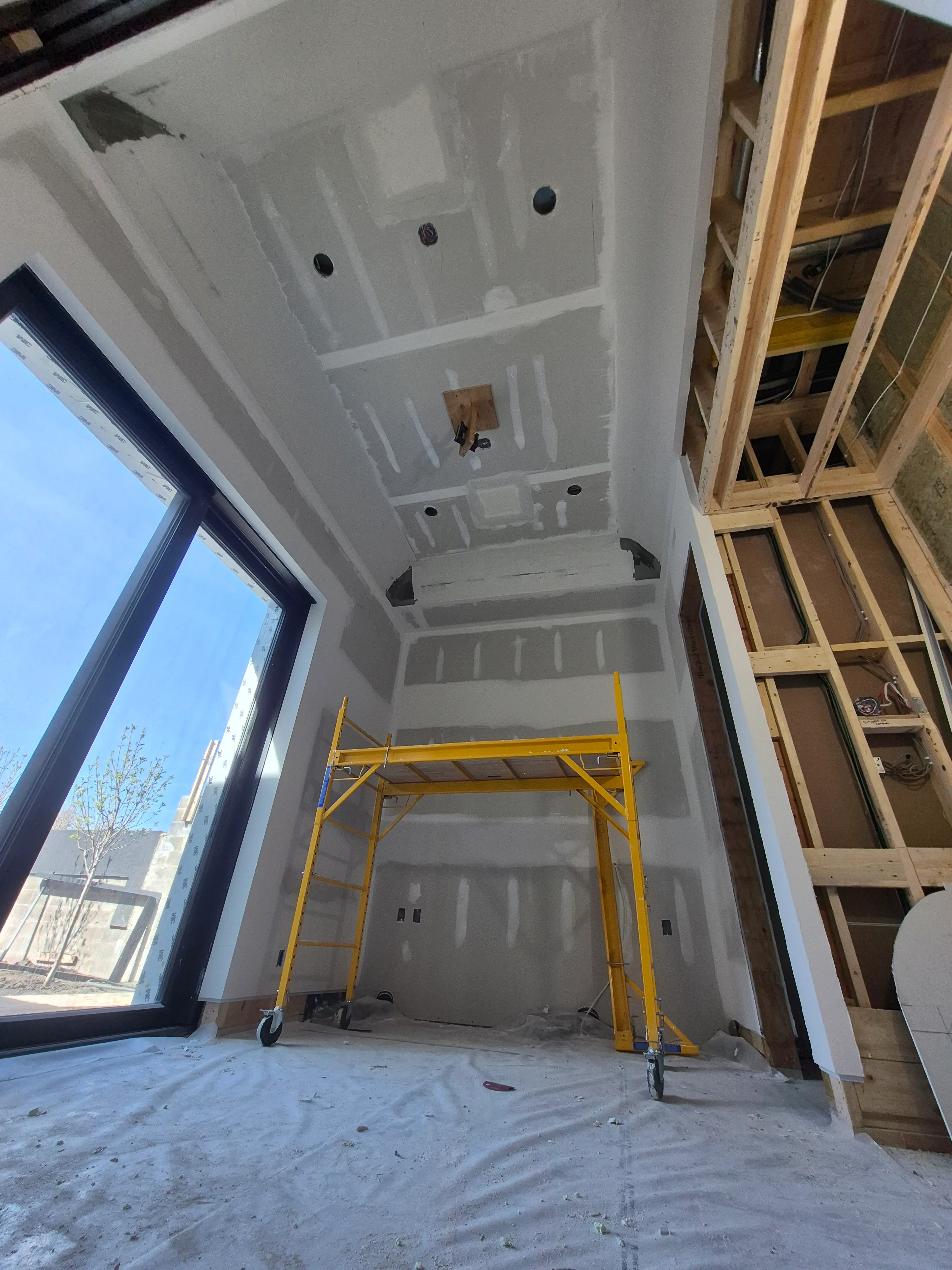 Construction worker installing insulation materials in an unfinished room with exposed wood framing and ceiling grid.