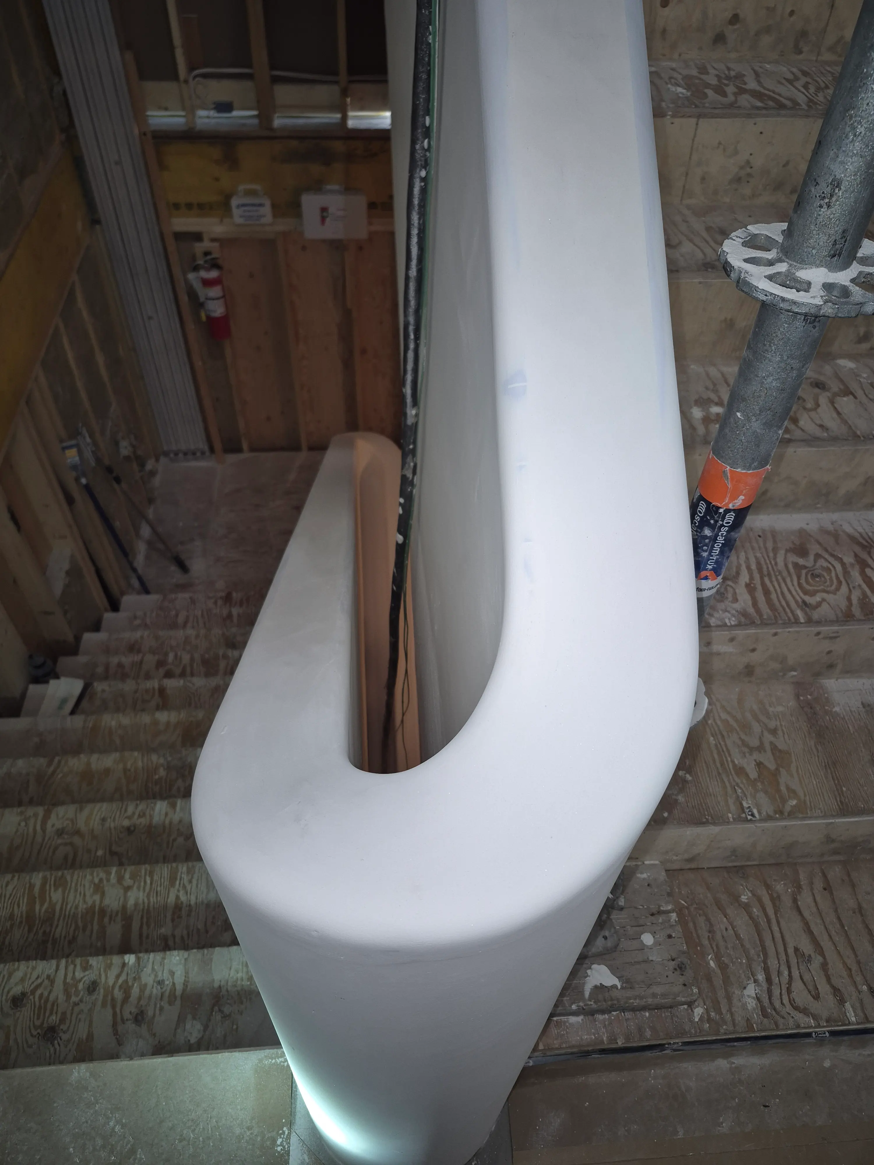 Smooth white curved handrail on a wooden staircase under construction with metal support poles.
